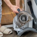 Female opening dust filter out of vacuum cleaner at home.