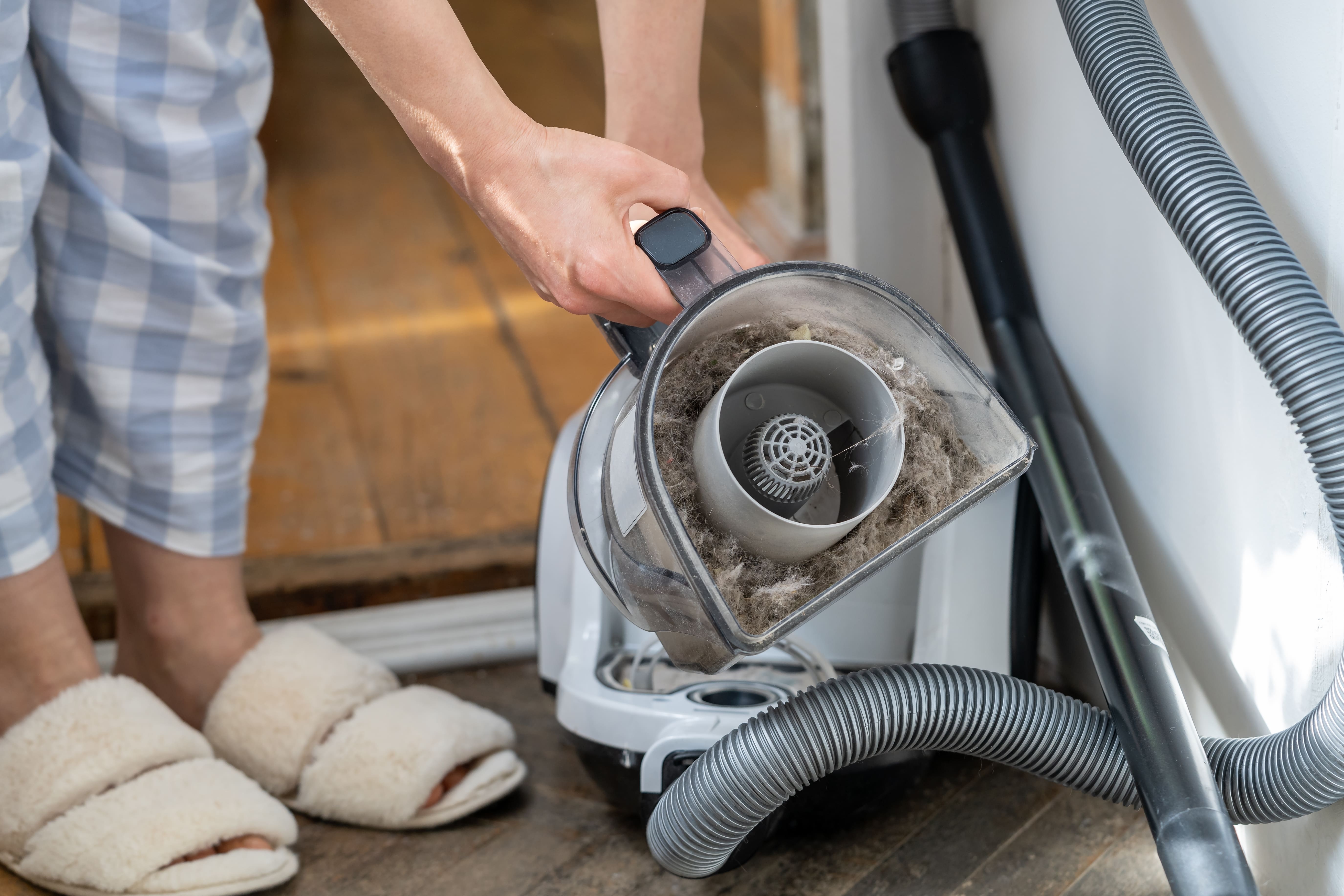 Female opening dust filter out of vacuum cleaner at home.